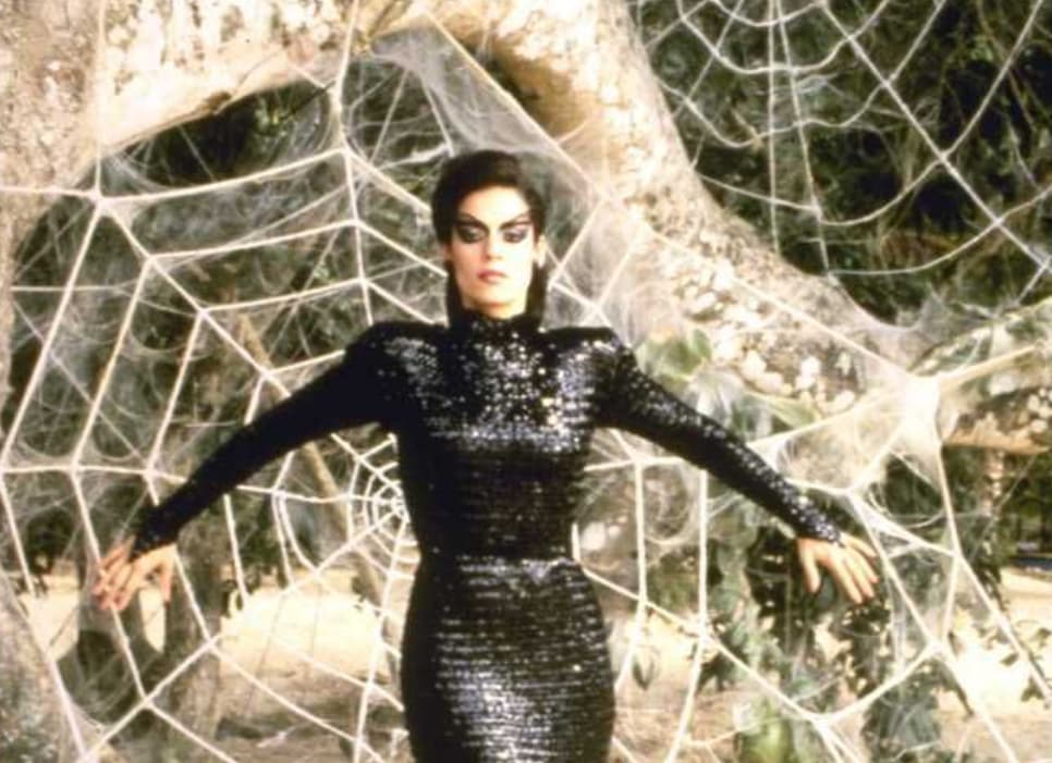 Woman in black sequined dress poses dramatically with a large spider web